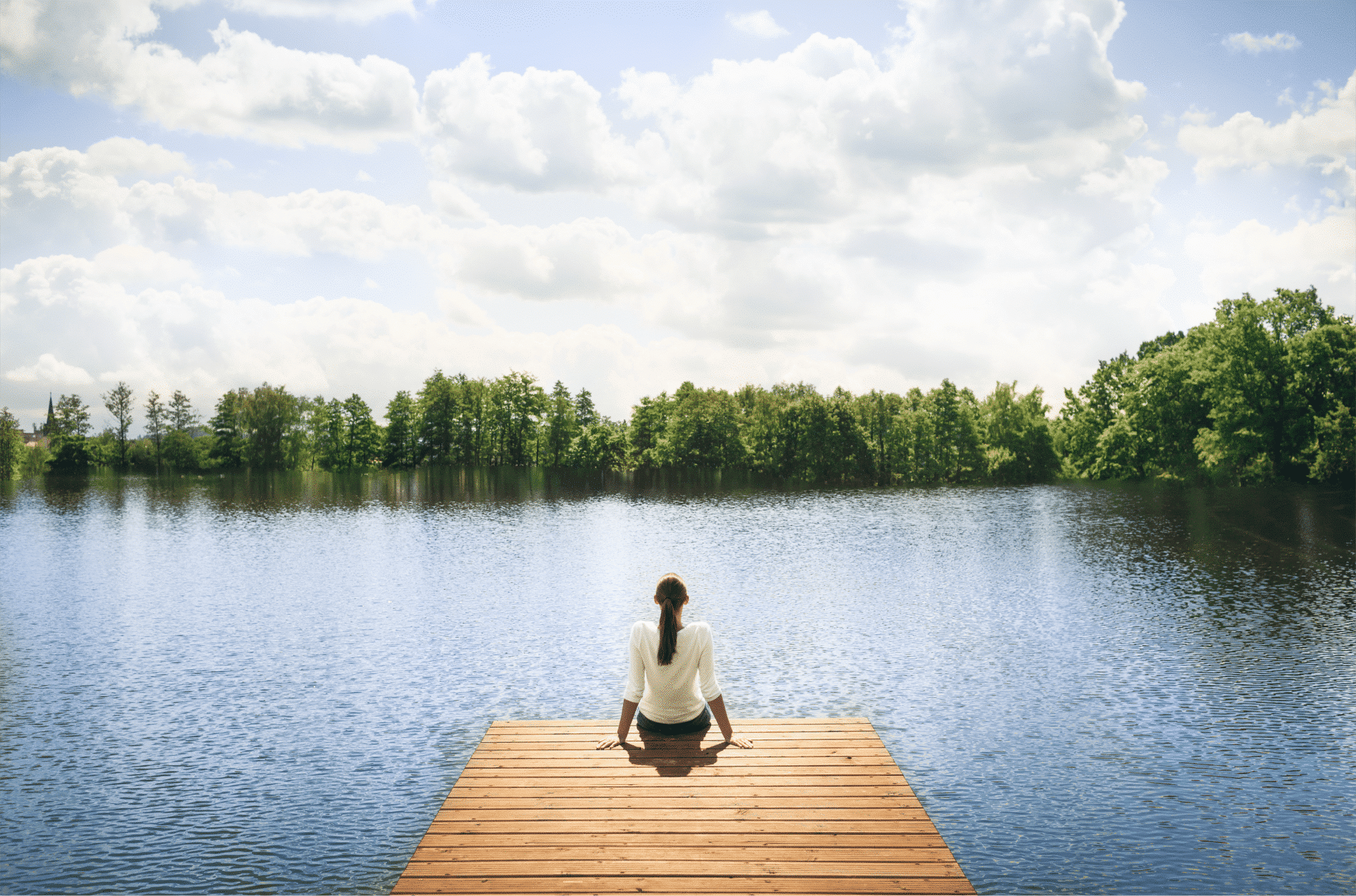Woman sitting on the end of a dock overlooking a lake while meditating